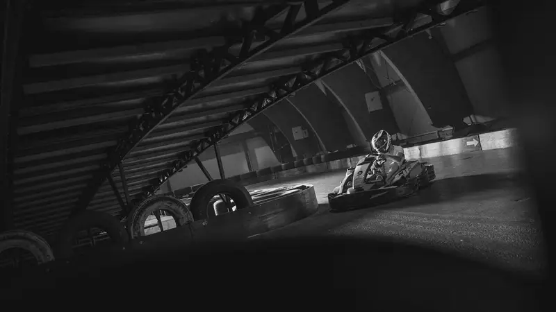 Kart on a dark indoor track under steel arches, with stacked tyres along the edge
